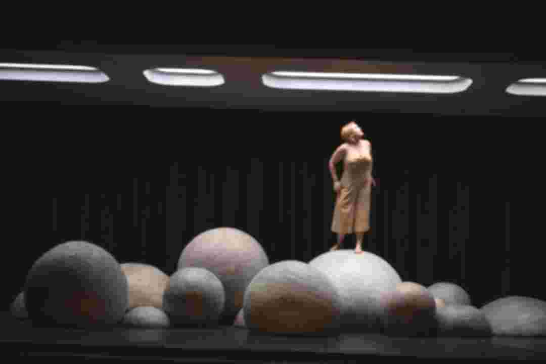 Ein dunkler Raum mit Leuchtfeldern an der Decke. Runde Felsen auf dem Boden. Eine Frau steht auf einem Felsen und blickt nach oben. © Sandra Then