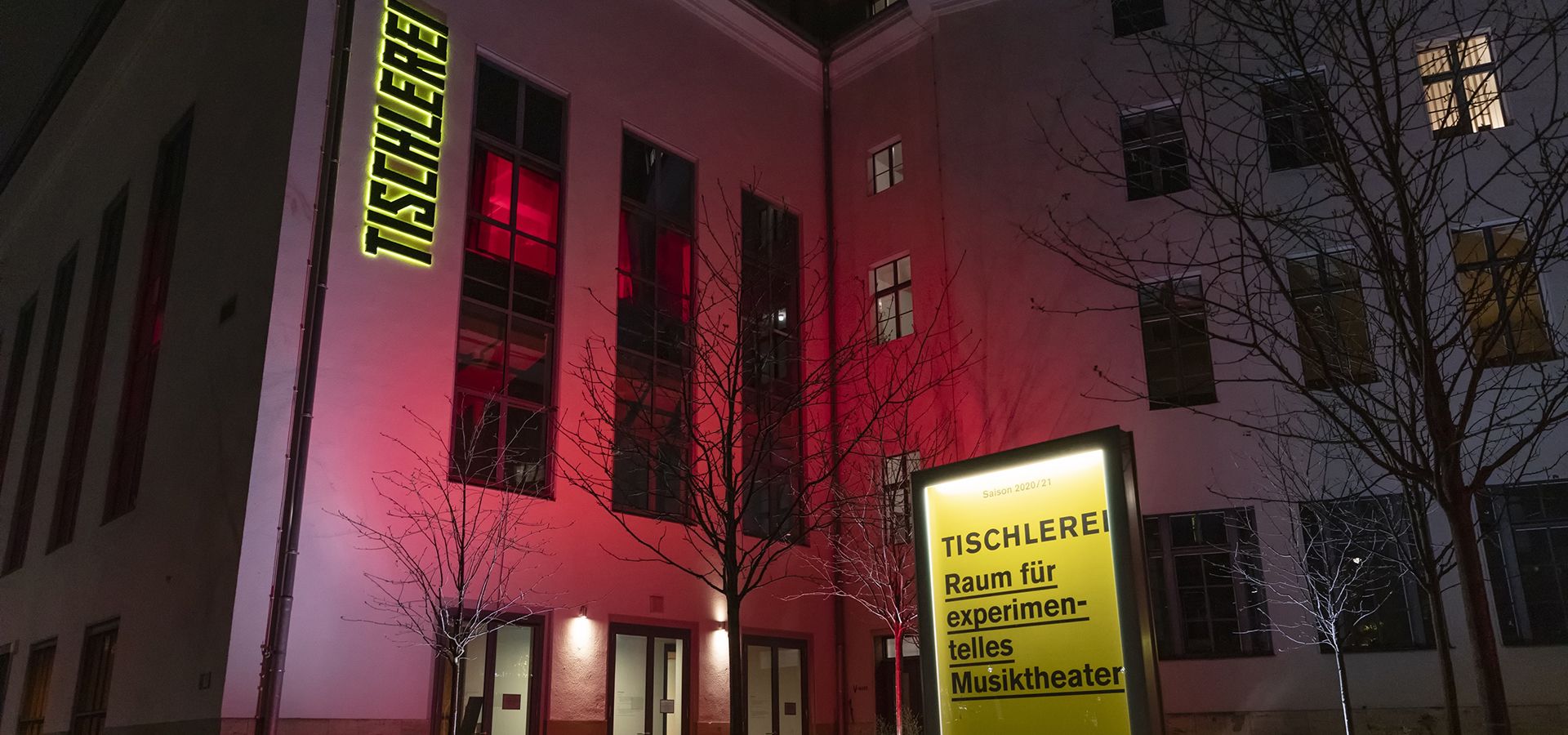 The Tischlerei – Space for New Music Theatre and Concerts Ein Foto der Tischlerei von außen bei Nacht. Sie ist leicht rot angestrahlt.