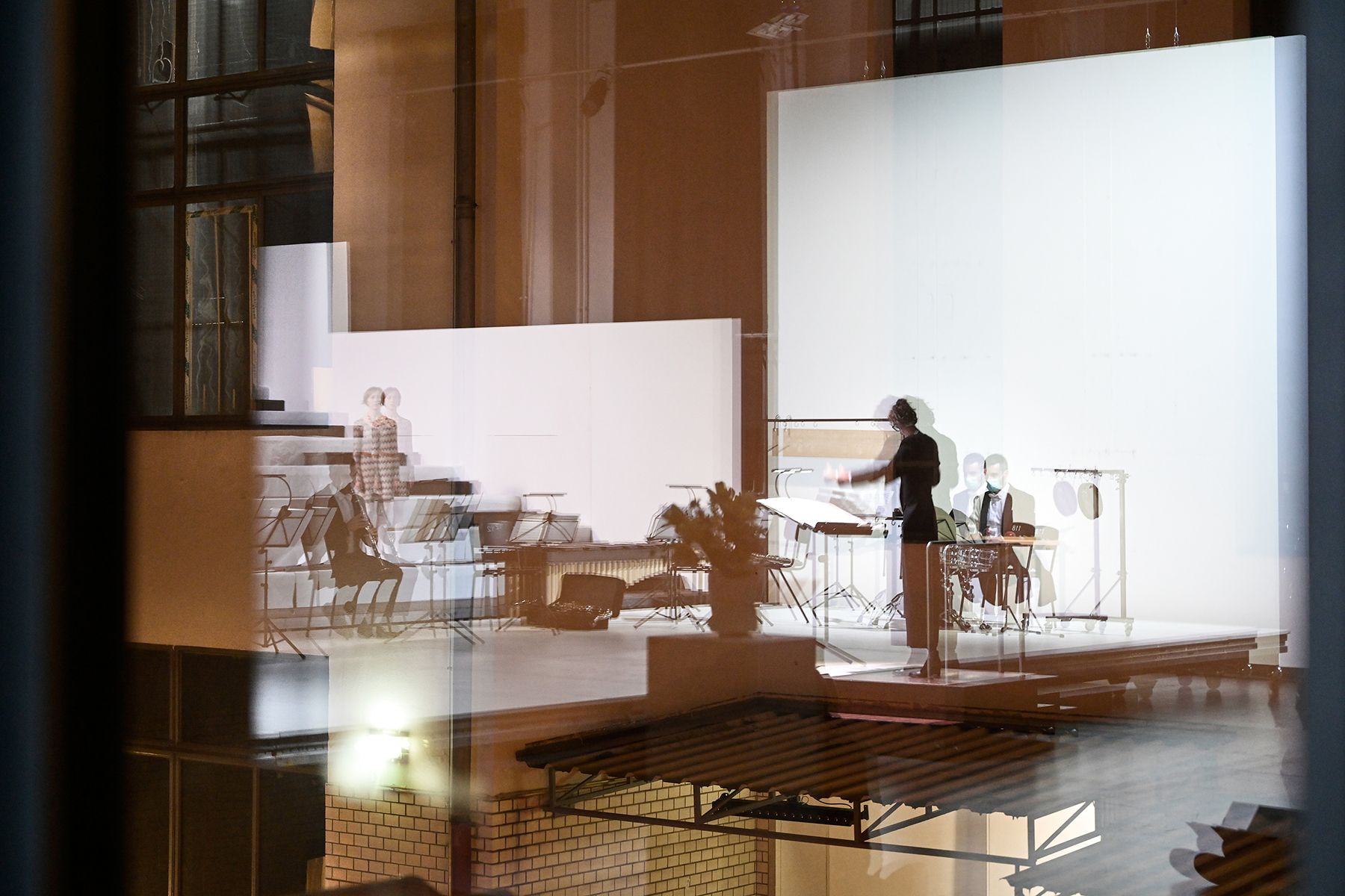 Die Tischlerei – Raum für neues Musiktheater und Konzert Auf diesem Foto vermischen sich in einer Art Überblendung architektonische Momente der Tischlerei mit Musiker*innen und einem Dirigenten. Es ist ein sehr atmosphärisches Bild, mit dem wir das Programm der Tischlerei bildlich fassen.